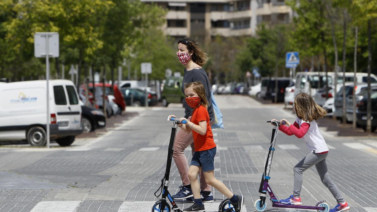 Dos niñas con mascarillas cruzan un paso de cebra montadas en patinete. Dos niñas con mascarillas cruzan un paso de cebra montadas en patinete.