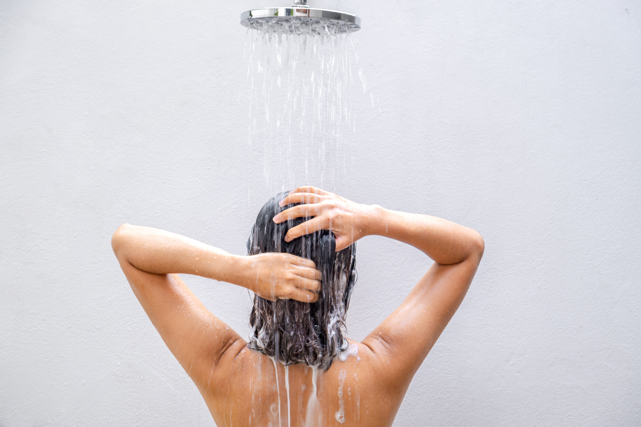 Mujer lavándose el pelo con champú en la ducha.