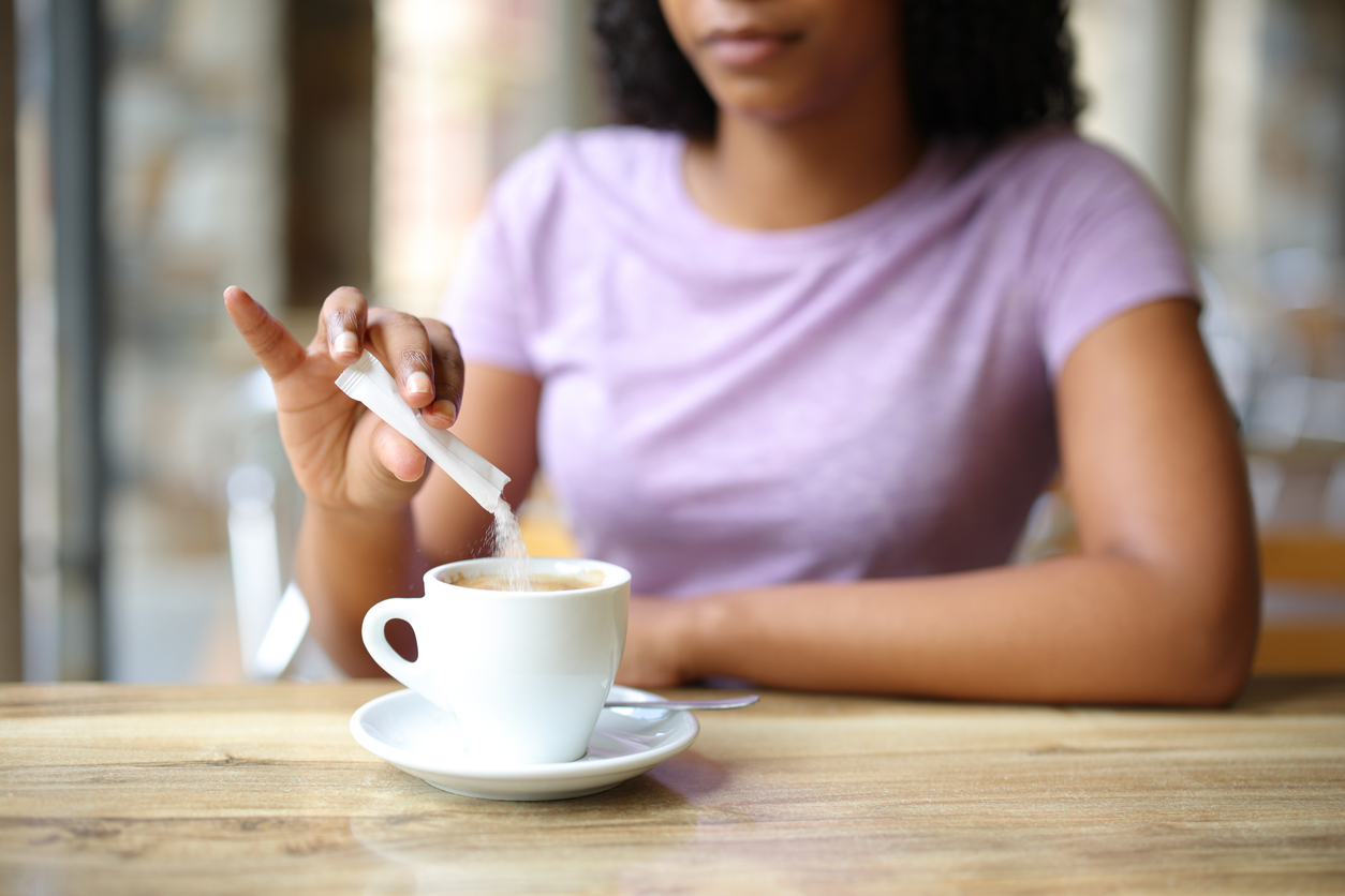 Mujer tomando café añadiendo un sobre de azúcar